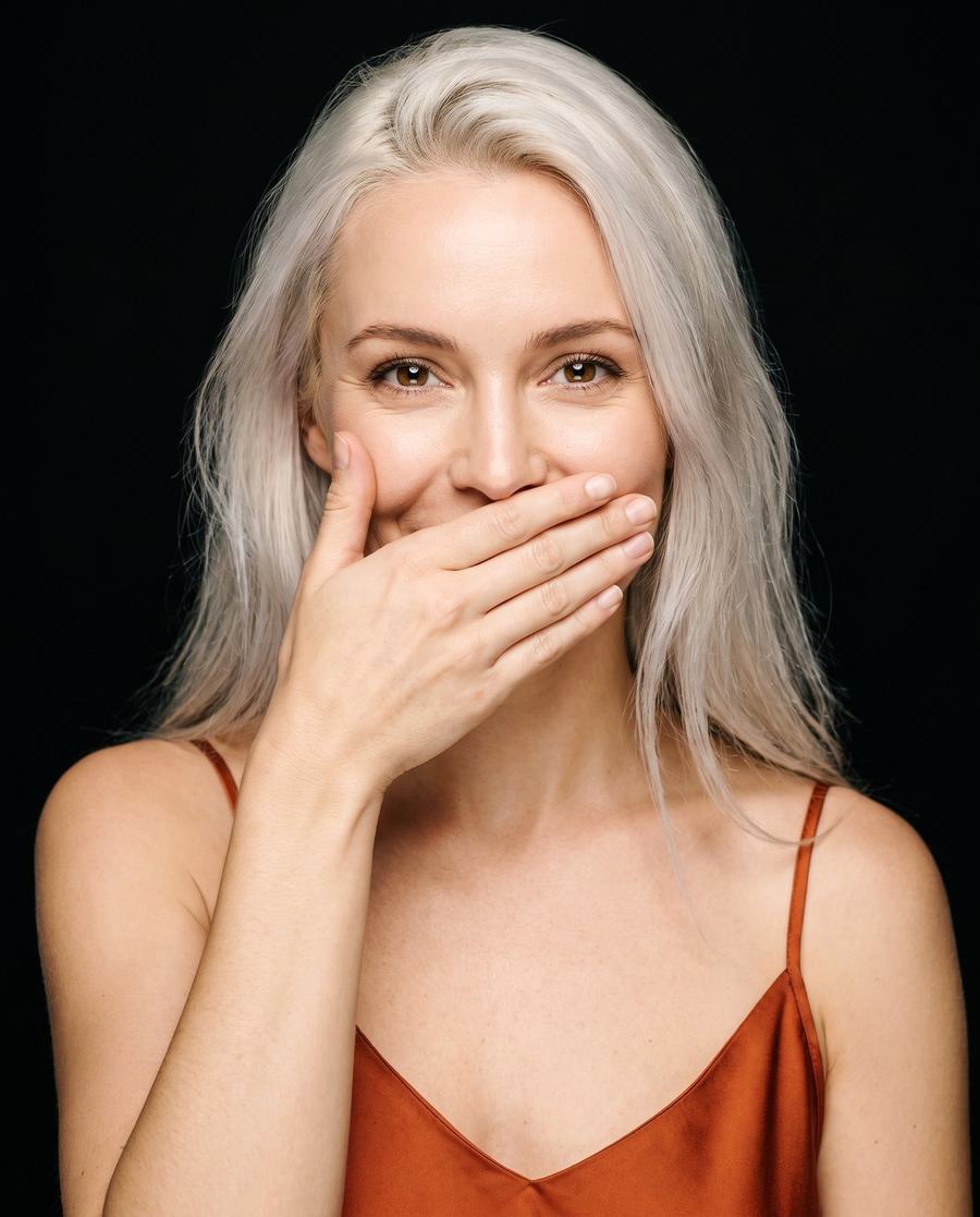 A woman with her hand over her mouth, laughing at what she is not saying.